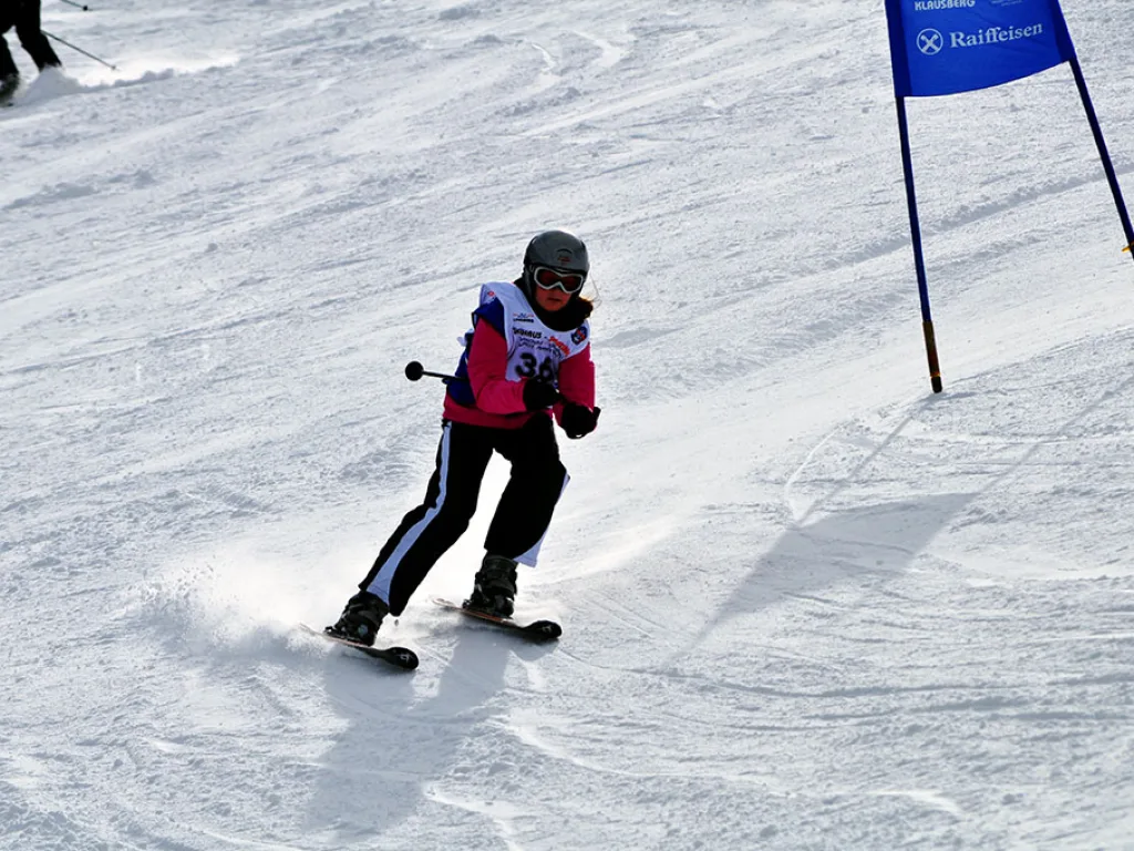 Skifahrerin fährt mit aufstiebendem Schnee auf das blaue Tor zu.